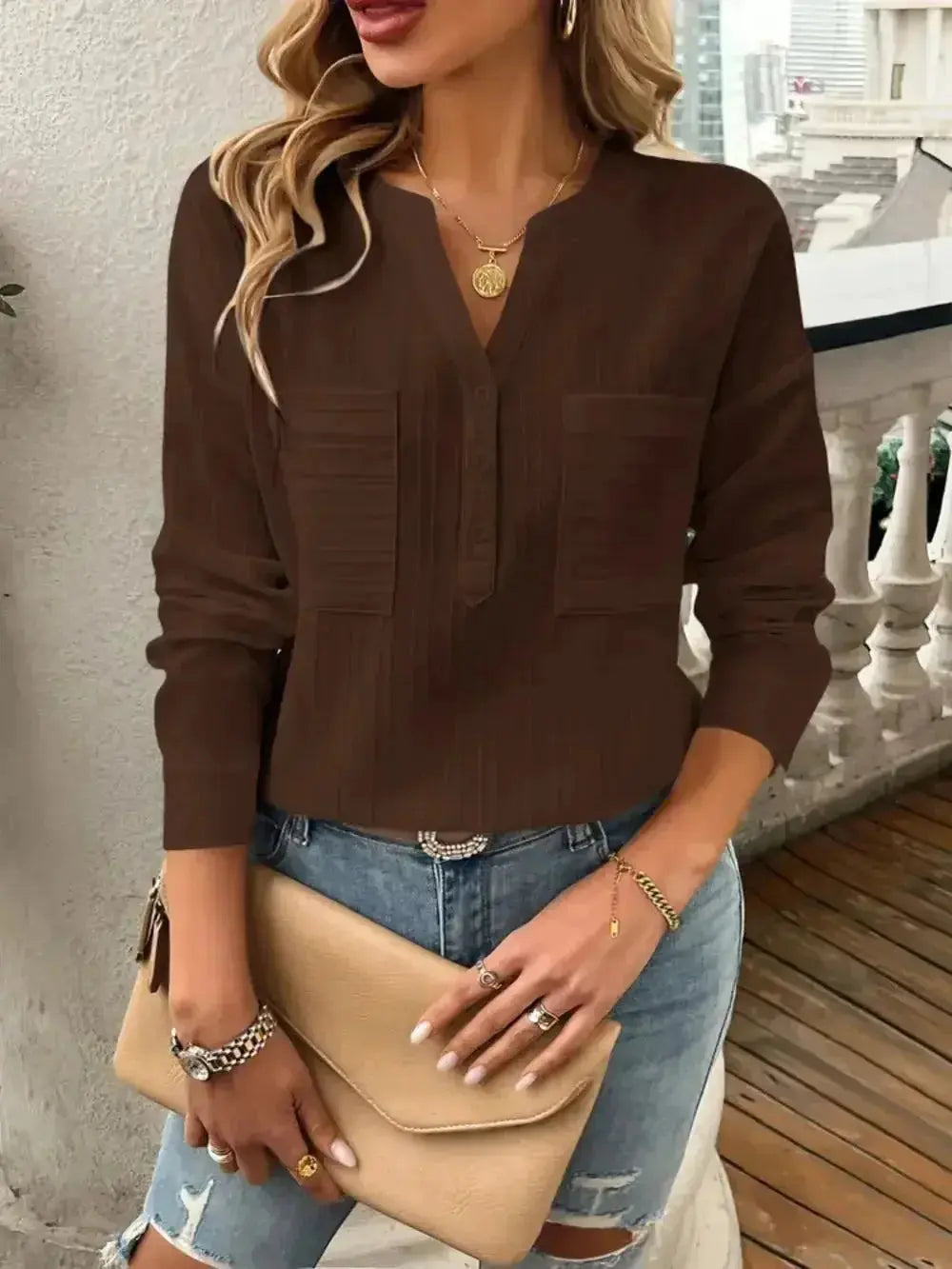 Brown V-neck blouse with front pockets, paired with ripped jeans and a beige clutch, modern minimalist style