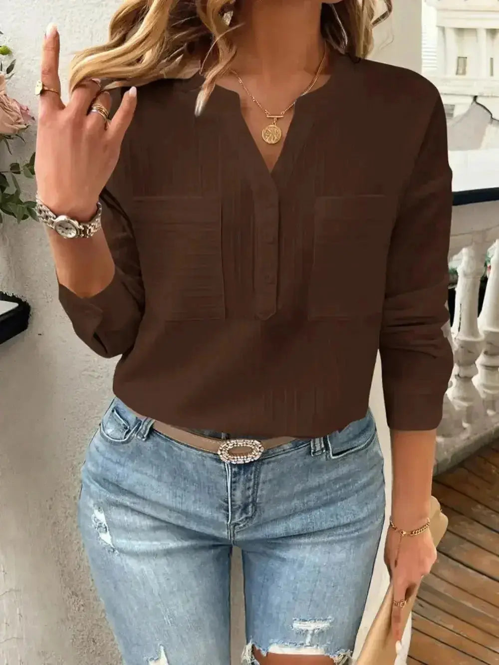 Brown V-neck blouse with front pockets paired with ripped jeans and gold accessories